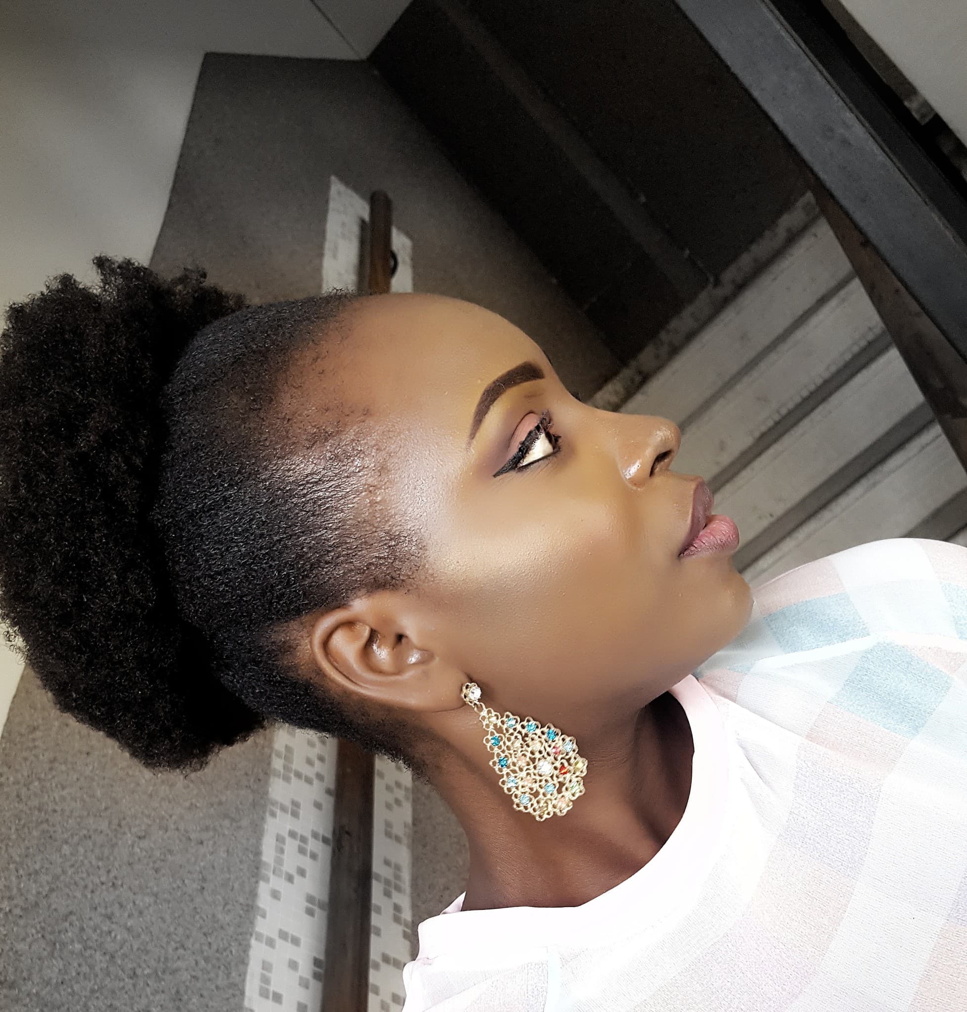 Client with a defined natural hair puff and gold statement earrings, styled at Baduwa Locs & Naturals